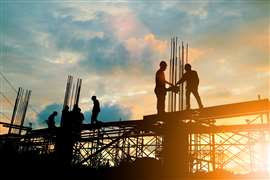 Construction workers and scaffolding in silhouette against a sunset