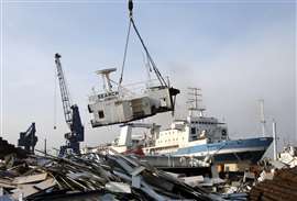 Part of a ship being lift by crane in a scrap yard