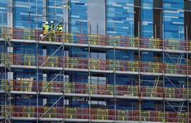 Construction workers on scaffolding inspect the facade of a high-rise building.