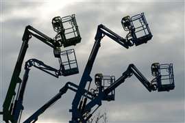 Silhouettes of boom lifts against dusk sky