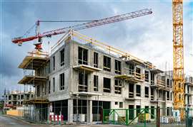 Un projet de construction résidentielle à ossature béton en Europe, avec une grue à tour jaune au premier plan à droite et une grue à tour rouge à l'arrière-plan à gauche.