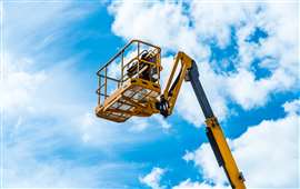 Hydraulic lift platform with bucket of yellow construction vehicle, blue sky and white clouds on background