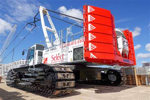 Rear three quarter view of red and white crawler crane with boom down