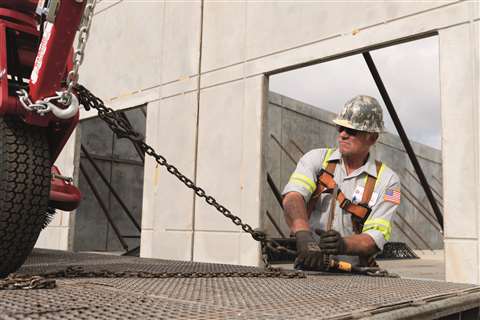 A worker secures a construction vehicle on a low-loader trailer